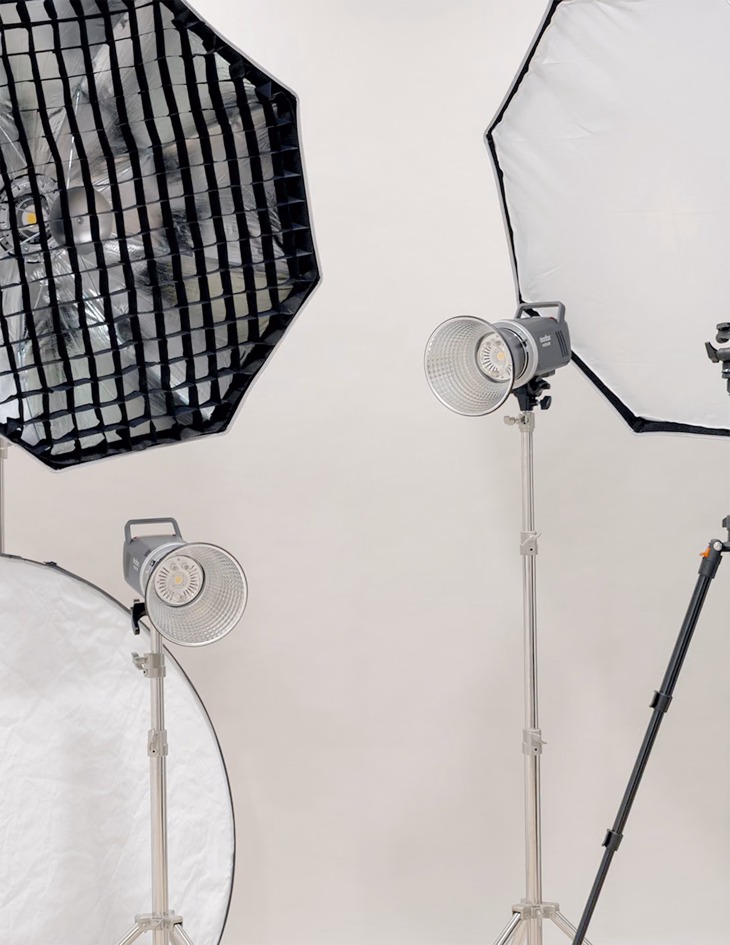 Four photography studio lighting equipment: two octagonal softboxes—one with a grid and the other without—and two light stands with mounted LED lights, set against a plain beige background.
