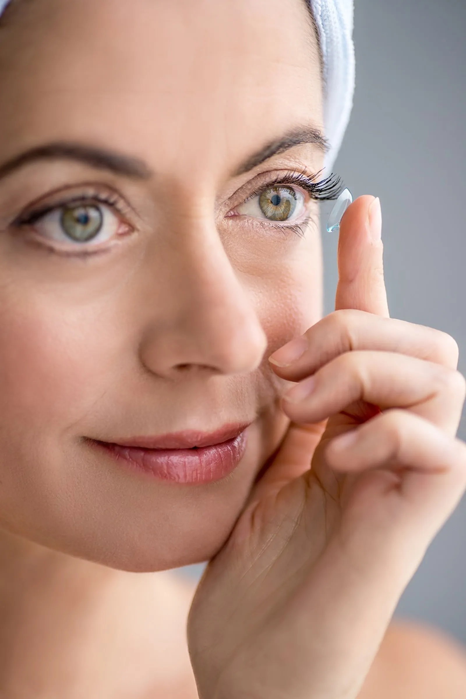 Close-up of a woman inserting a contact lens into her eye.