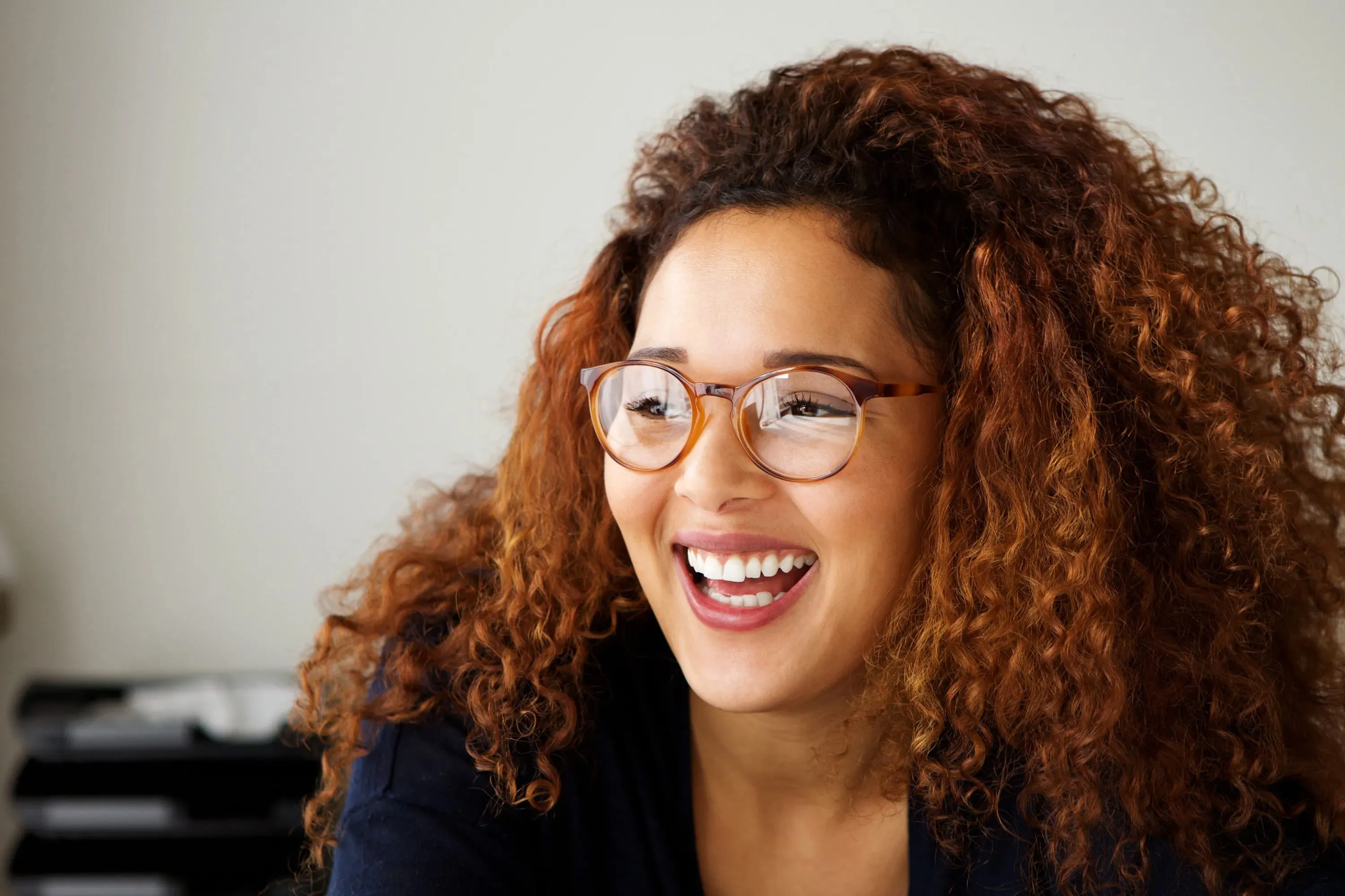 Smiling woman with curly red hair wearing glasses looking to the side.