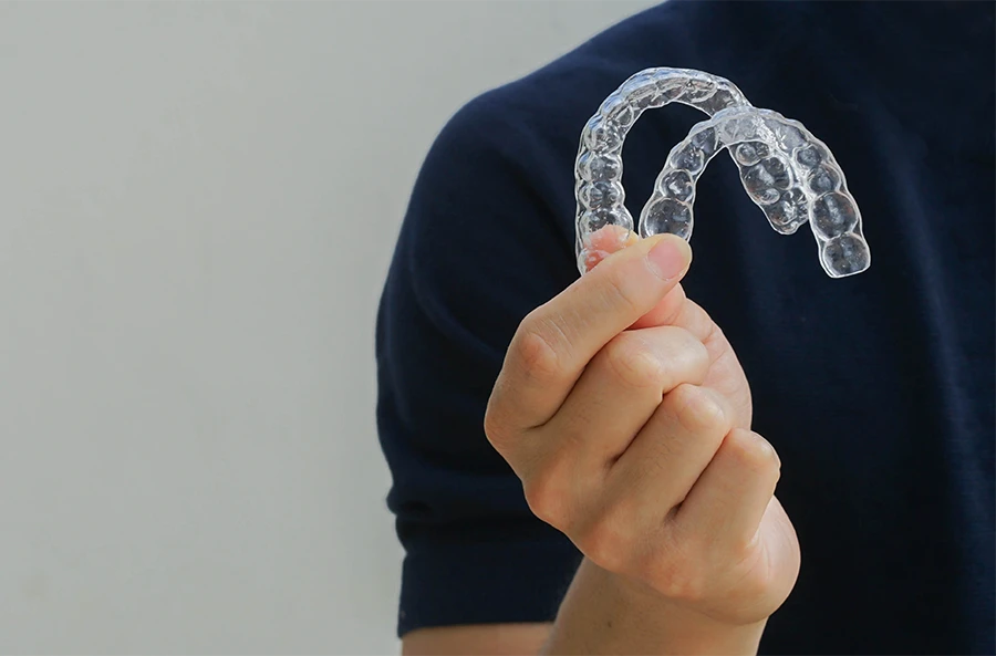 Person holding two clear dental aligners between thumb and forefinger.