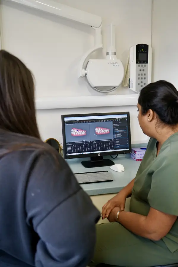 Two women looking at dental scan images displayed on a computer screen in a clinical setting.