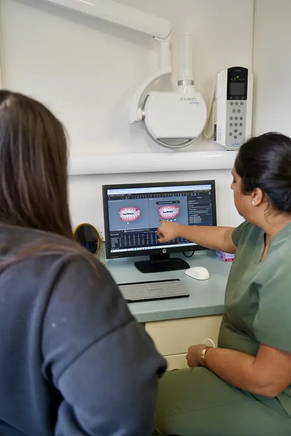 Dental professional in green scrubs showing a dental X-ray on a computer screen to a patient.