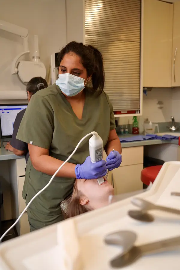 Dental professional wearing a face mask and gloves using an intraoral scanner on a patient reclining in a dental chair.