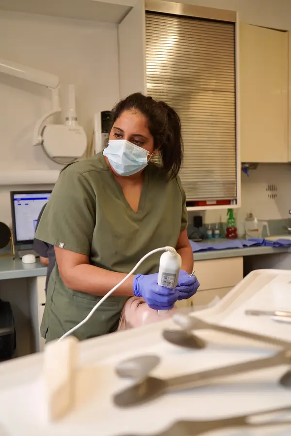 Healthcare professional in green scrubs and blue gloves using an ultrasound device on a patient's face in a medical office.