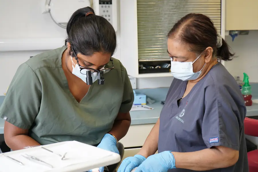 Two female dental professionals wearing masks and gloves working together in a clinic.