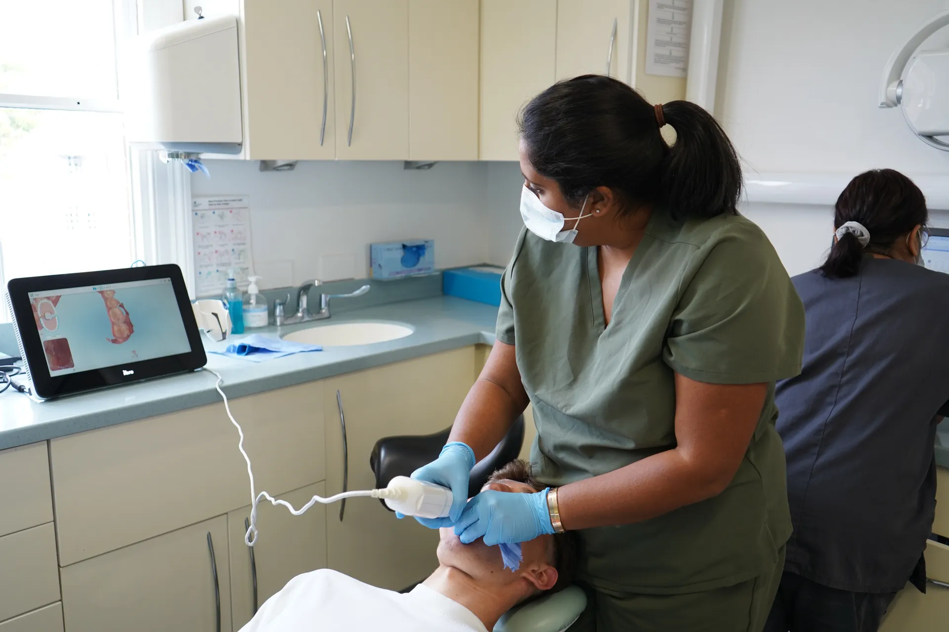 Dentist wearing a mask and gloves using a digital scanner on a patient's teeth in a dental clinic.