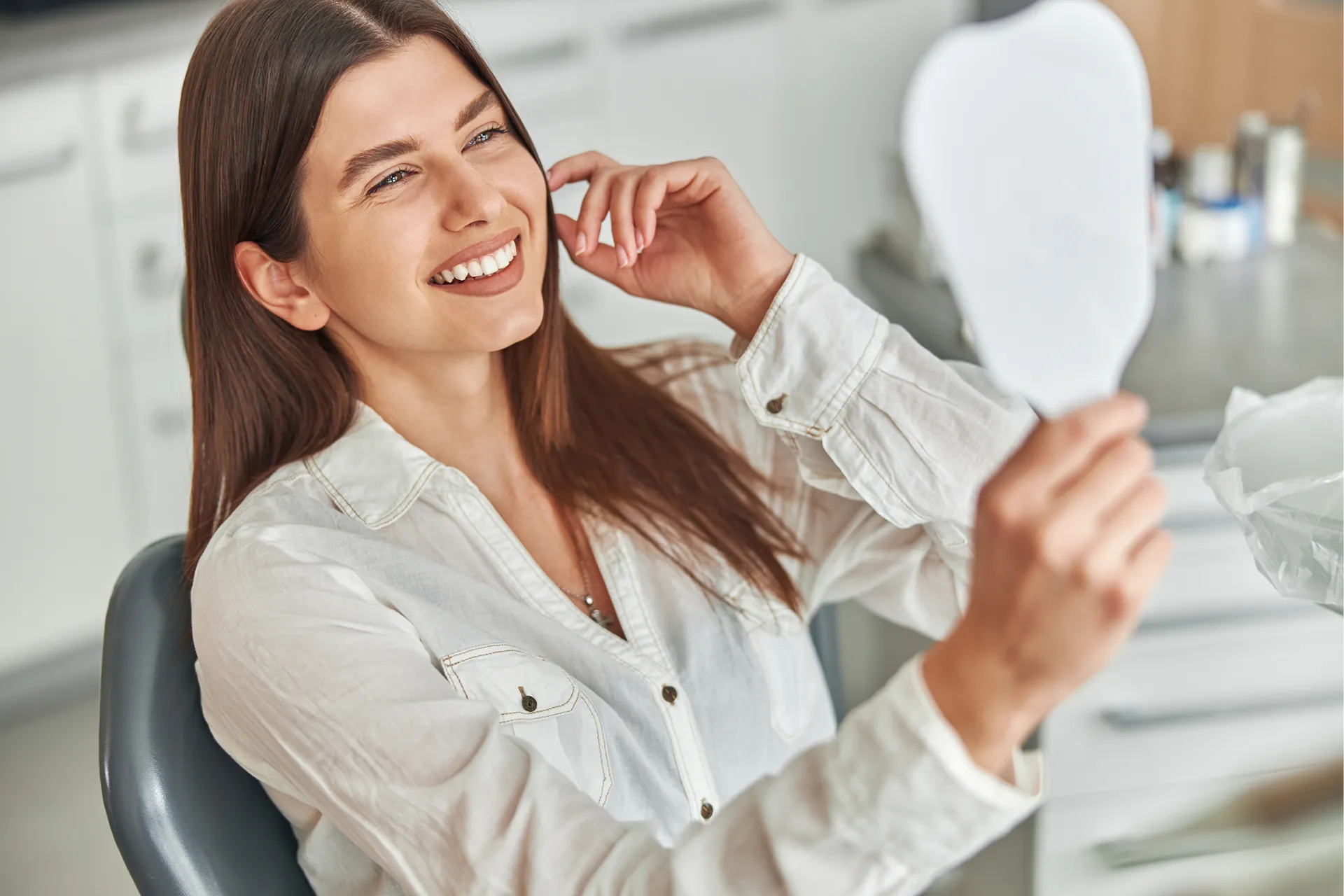 Young woman smiling and looking at her reflection in a handheld mirror.