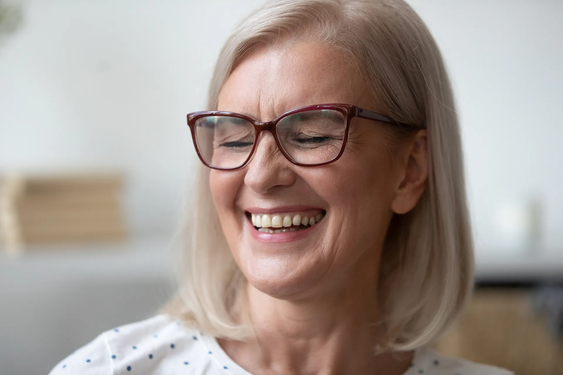 Close-up of a smiling elderly woman with short gray hair and glasses, eyes closed in joy.