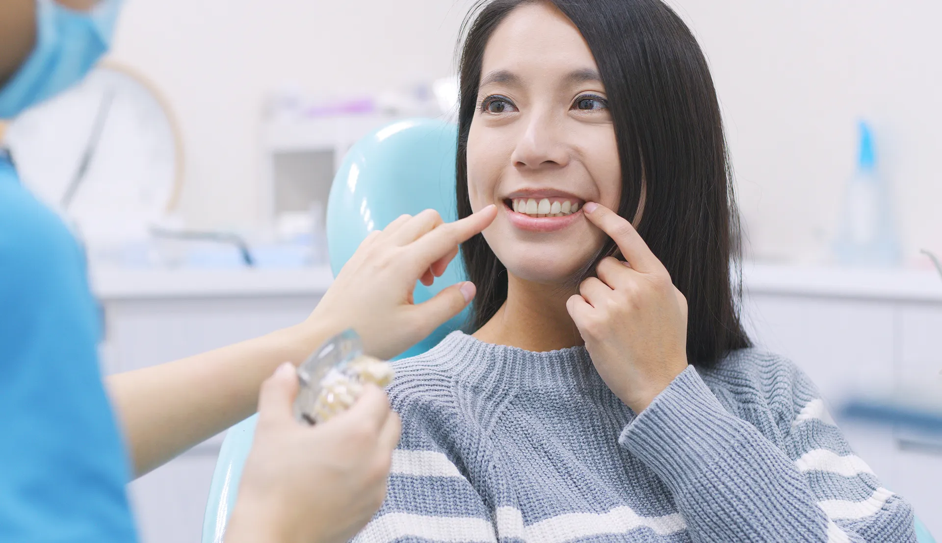 Dentist pointing at a woman's teeth while she smiles and touches her smile in a dental office.