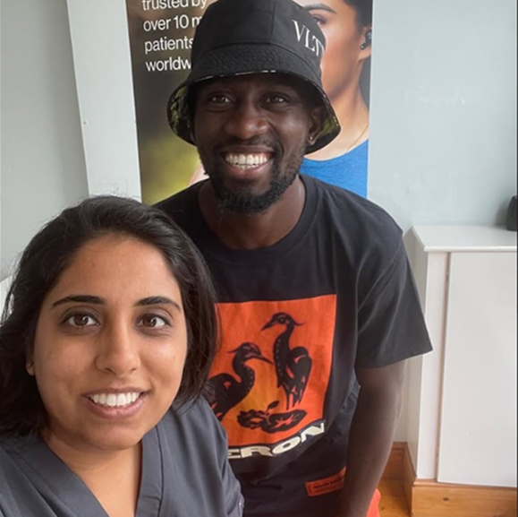 Smiling man wearing a black bucket hat and graphic t-shirt posing with a woman in a gray top.