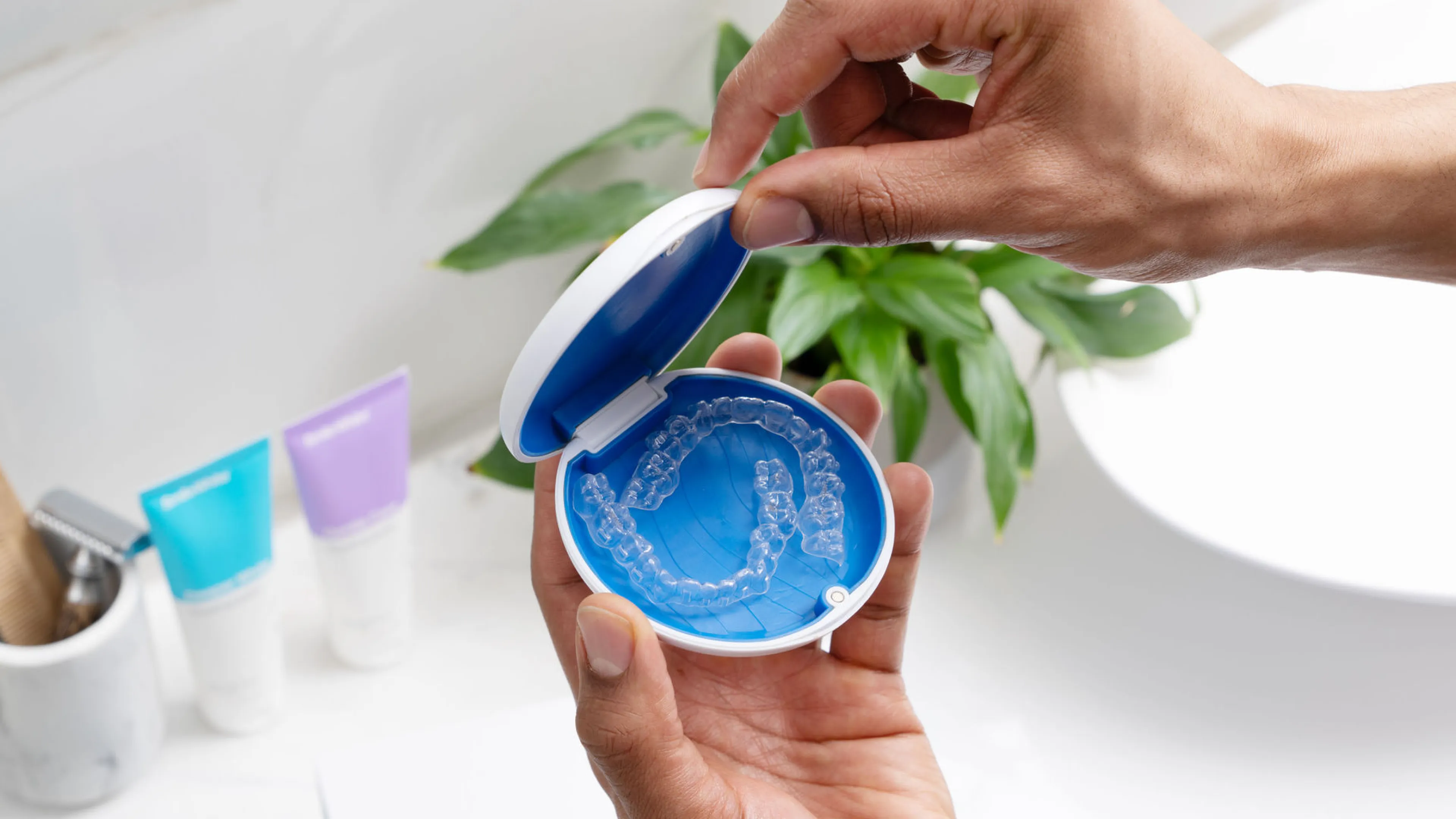 Hand holding an open blue and white case containing clear dental aligners.