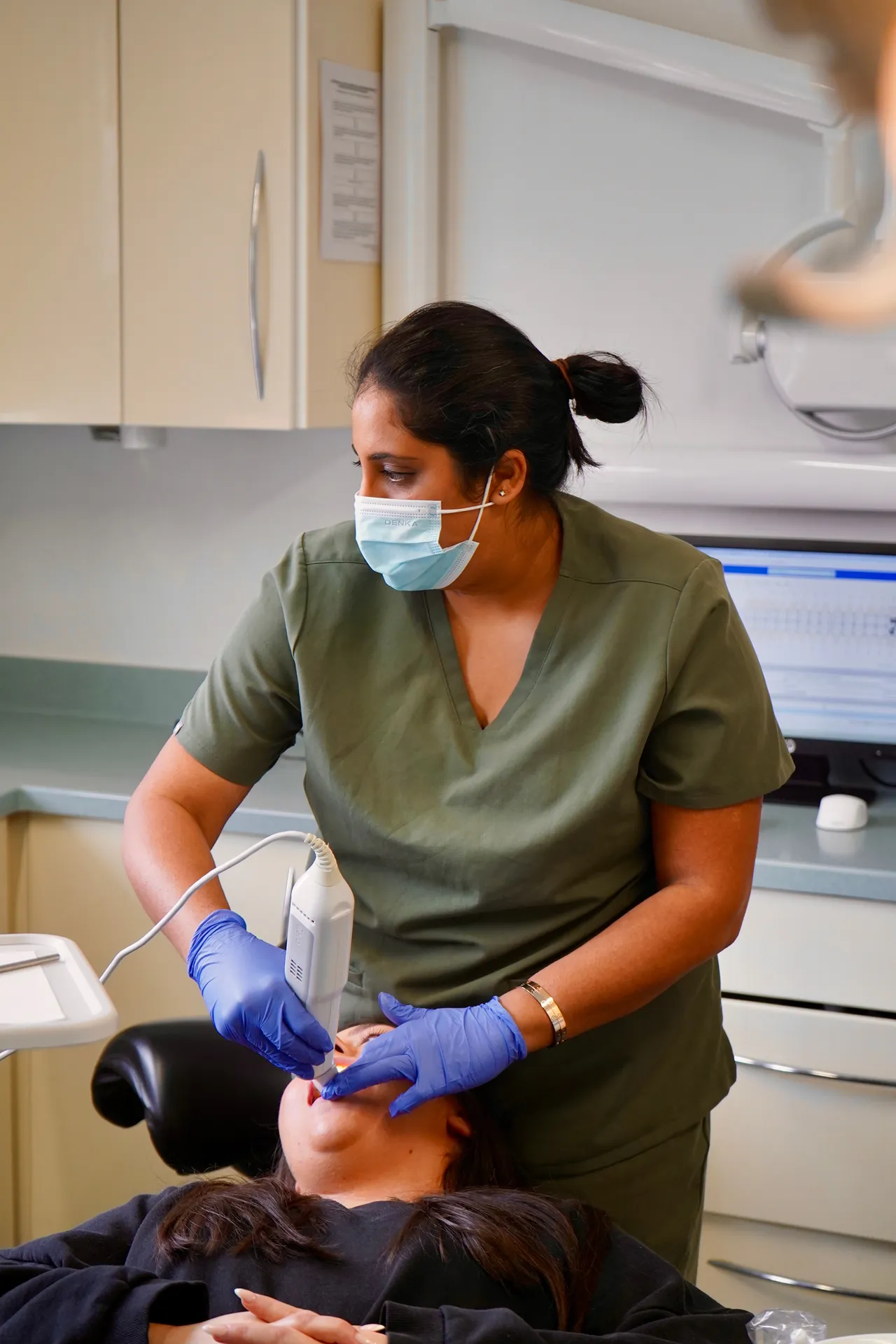 Female dental professional wearing gloves and a mask using a digital scanner inside a patient's mouth in a dental clinic.
