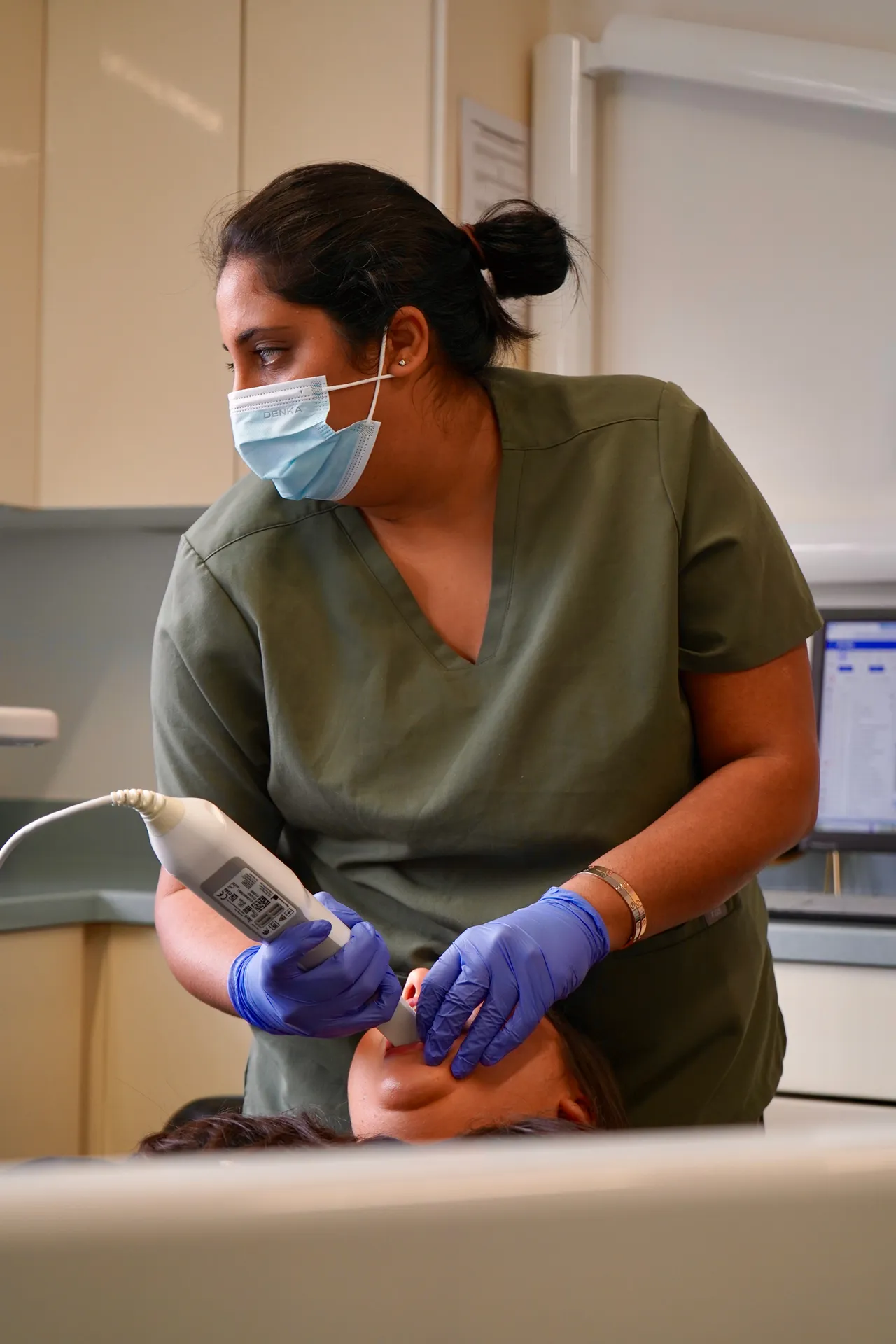 Dental professional wearing a mask and gloves using an intraoral scanner on a patient lying back in a dental chair.
