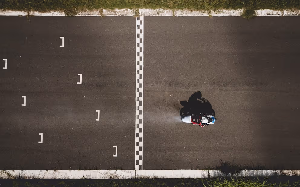 A person riding a motorcycle crossing a checkered finish line on an asphalt road, viewed from above.