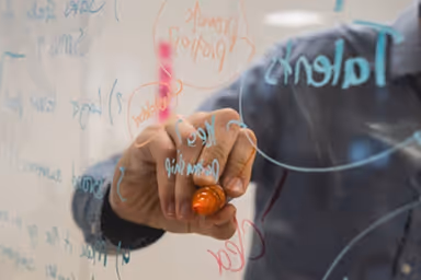 Person writing colorful notes and diagrams on a transparent glass board with a marker.