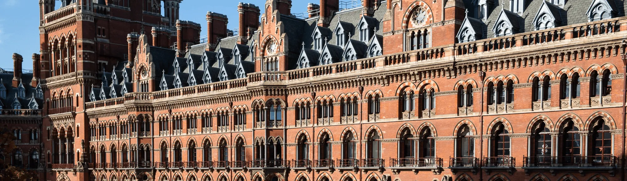 Detailed façade of a historic red brick building with tall chimneys and rows of arched windows under a clear blue sky.