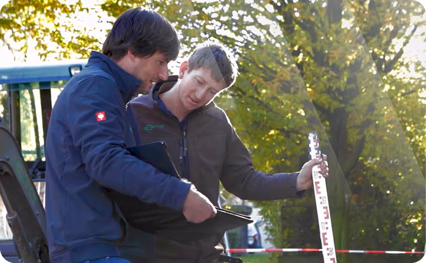 Zwei Männer im Freien besprechen Daten, einer hält ein Messlatten-Standardwerkzeug, der andere ein Tablet.