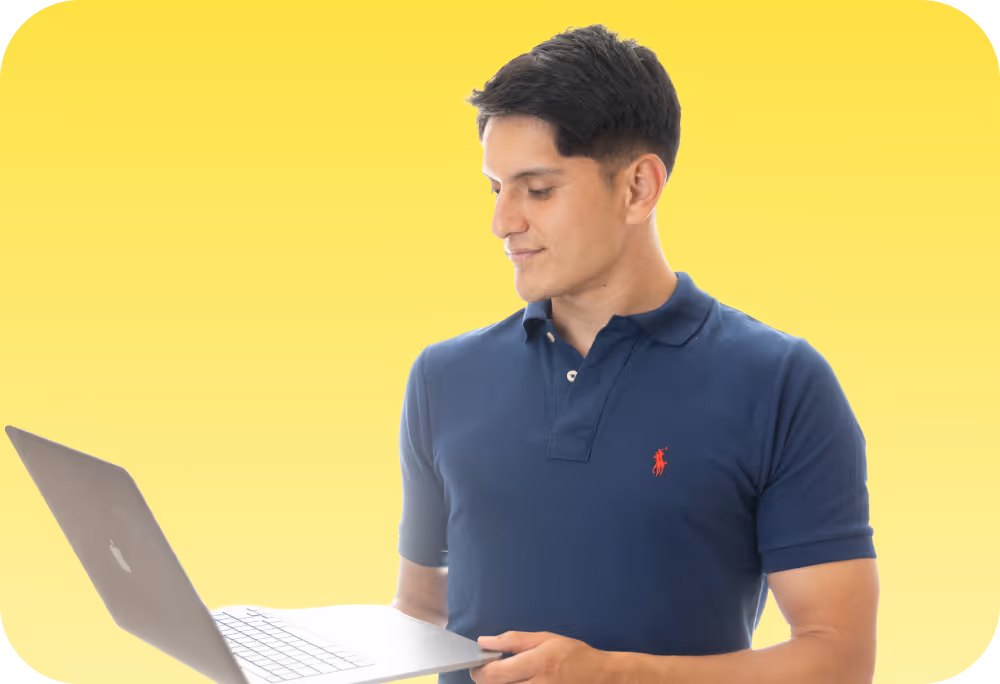 Junger Mann mit blauem Poloshirt hält Laptop vor gelbem Hintergrund.