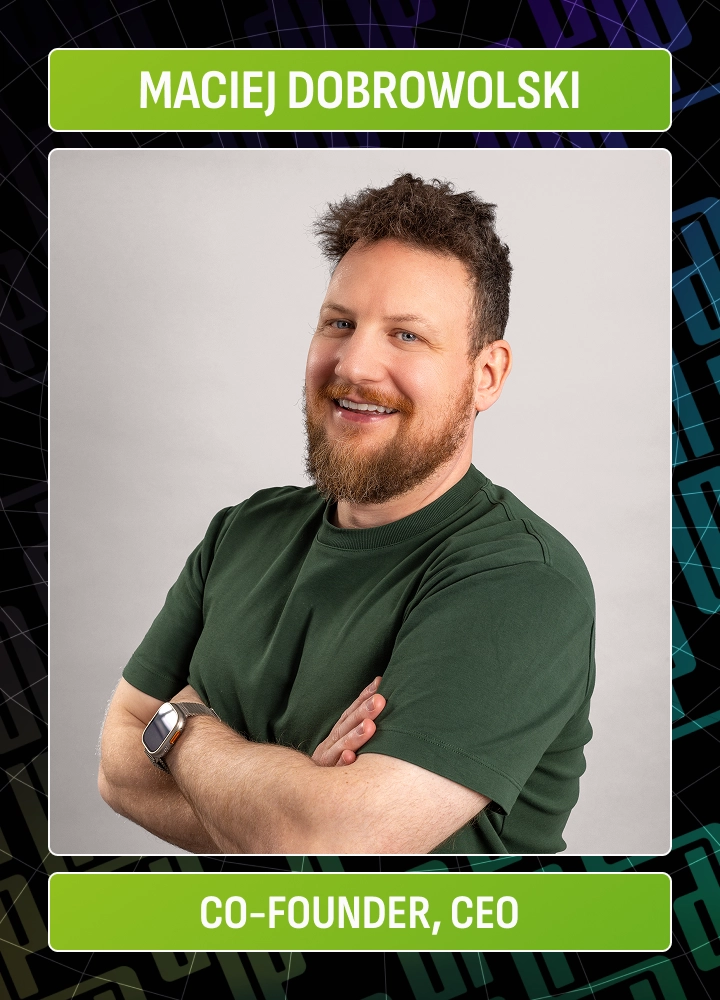 Man with beard and curly hair wearing a green shirt and smartwatch smiling with arms crossed.