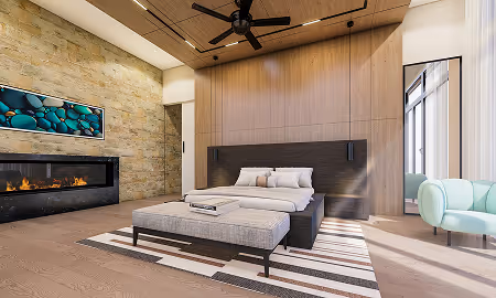Modern bedroom with a stone fireplace, large bed with bench, ceiling fan, wooden ceiling, and a light blue armchair near a tall window.