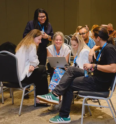 Testlio team sitting in a circle, engaged in a discussion with one person showing something on a laptop.