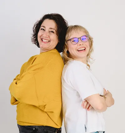 Testlio employees standing back to back, smiling and crossing their arms, one in a mustard yellow sweater and the other in a white shirt with glasses.