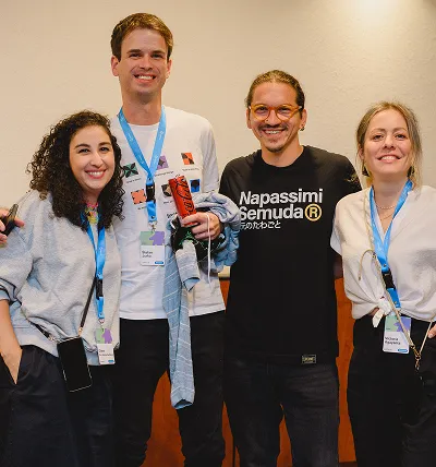 Testlio employess standing close together, wearing conference badges and casual clothing with two men and two women.