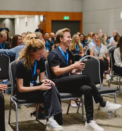 Testlio team in a conference room, two attendees in front laughing and holding a microphone.