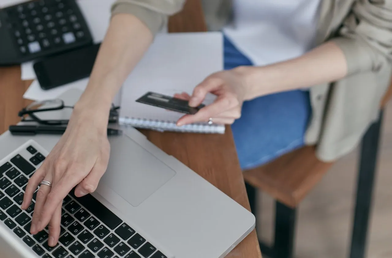 Close-up photo of a woman holding a credit card and typing on her laptop