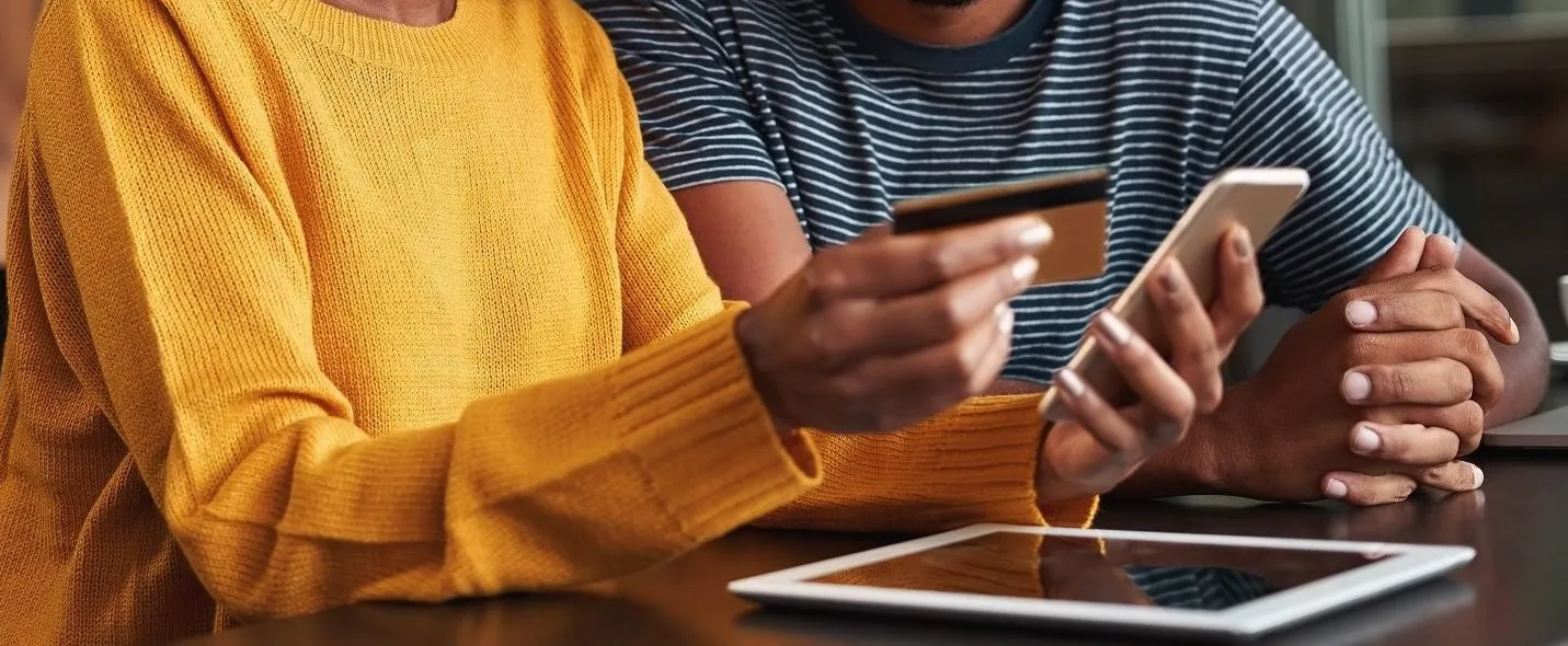 Close-up photo of a woman holding a credit card and a phone with a man by her side