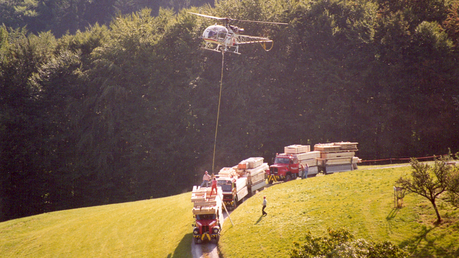 Historische Aufnahme: Helikopter transportiert Holzelemente auf eine Baustelle