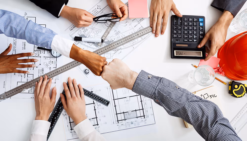 Group of people collaborating on architectural plans with rulers, calculator, and safety helmet on the table.