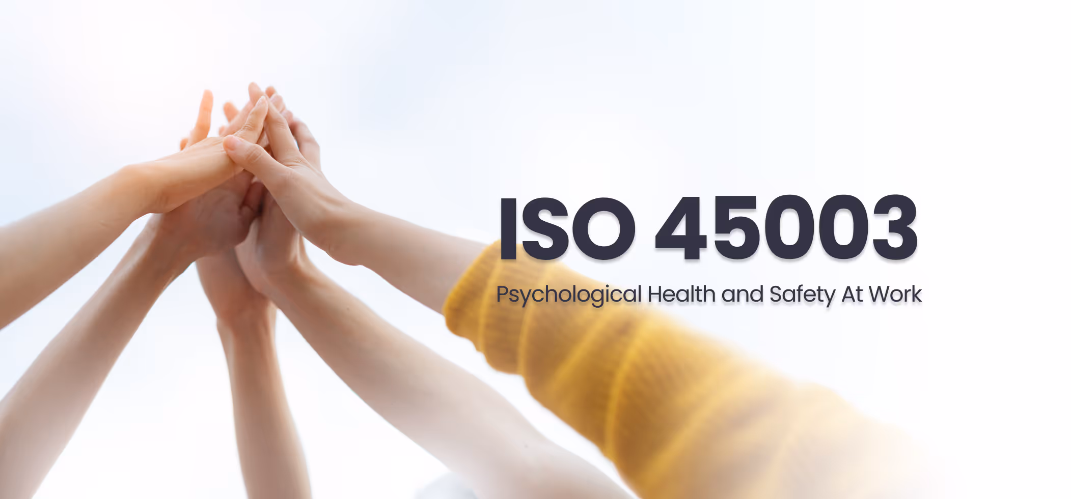 Group of hands stacked together in a team gesture with text 'ISO 45003 Psychological Health and Safety At Work' on a light background.