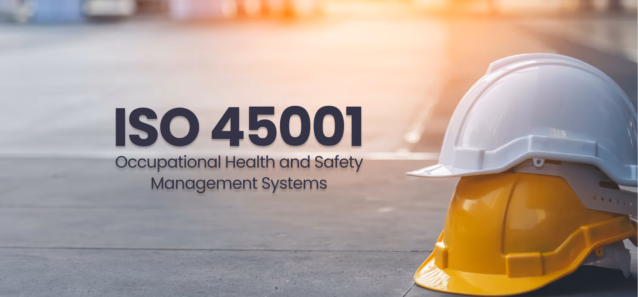 Text 'ISO 45001 Occupational Health and Safety Management Systems' beside stacked white and yellow safety helmets on a concrete floor with a soft light background.