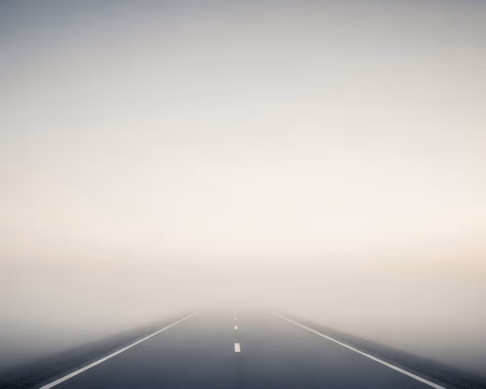 Empty road fading into dense fog, limiting visibility.
