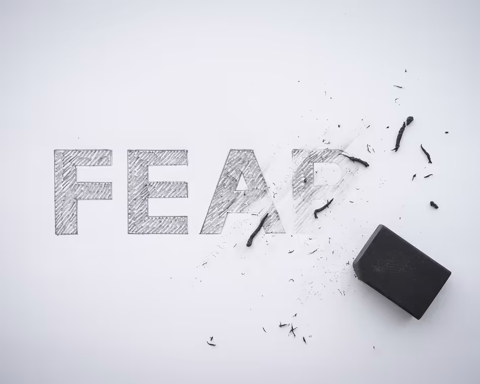 The word 'FEAR' partially erased on a white surface with a black eraser and eraser debris visible.