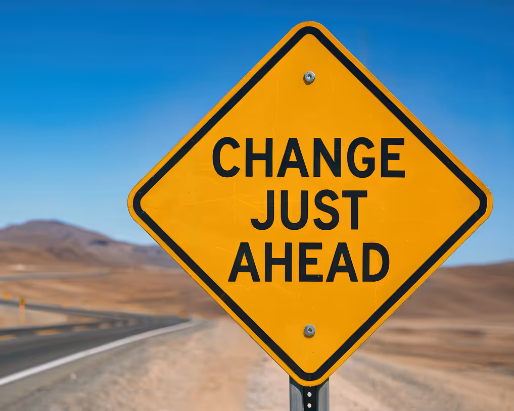 Yellow diamond road sign with black text reading 'CHANGE JUST AHEAD' against a clear blue sky and desert landscape.