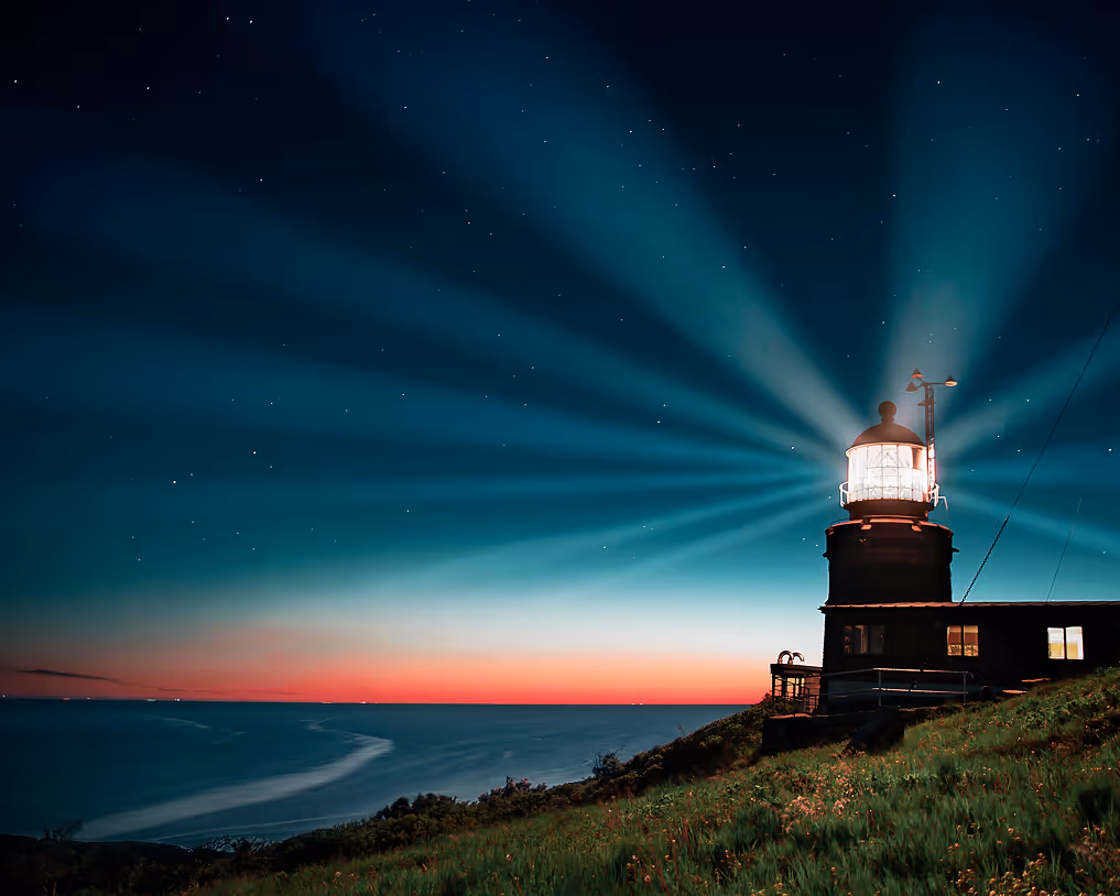 Lighthouse shining beams across a dark blue night sky with stars and a distant red horizon over a calm sea.