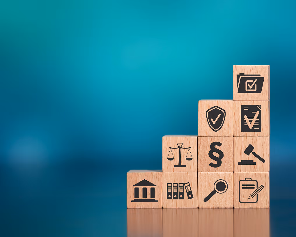 Stacked wooden blocks with legal symbols including courthouse, files, scales of justice, paragraph sign, magnifying glass, clipboard, gavel, shield with check mark, document with check mark, and folder.