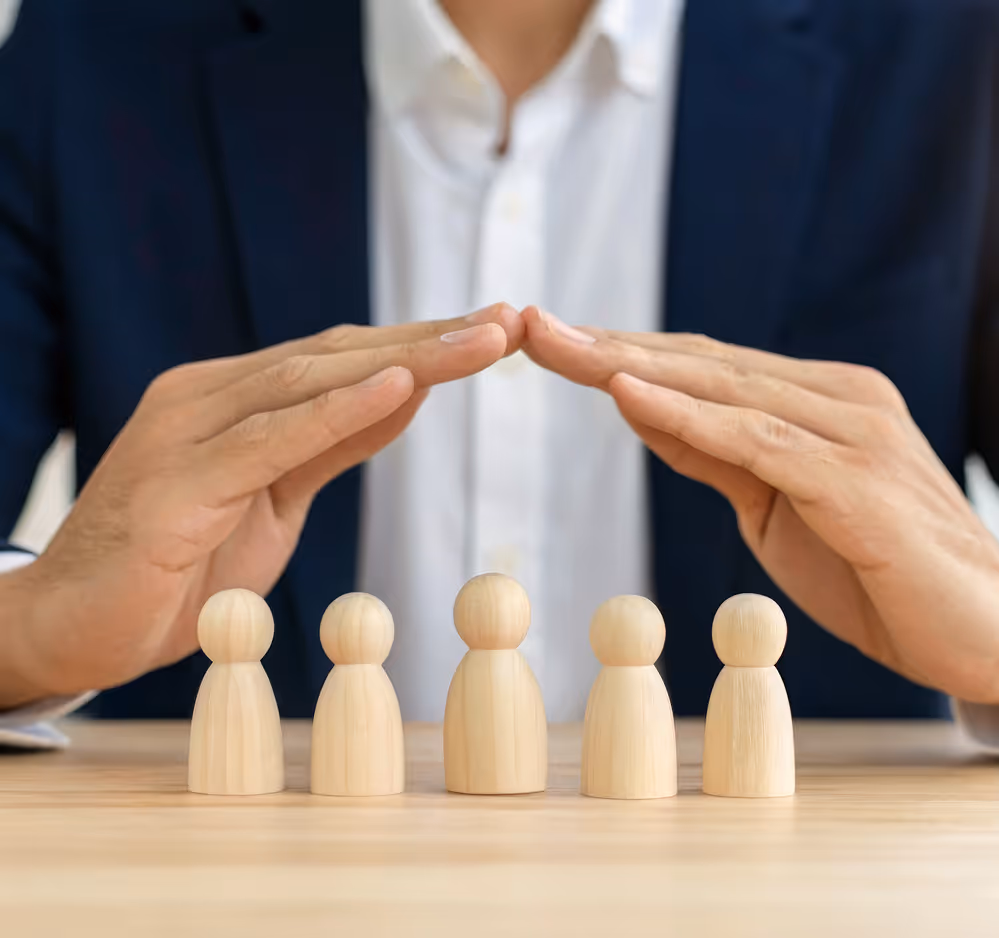 Hands forming a protective gesture over five wooden human-shaped figures lined up on a table.