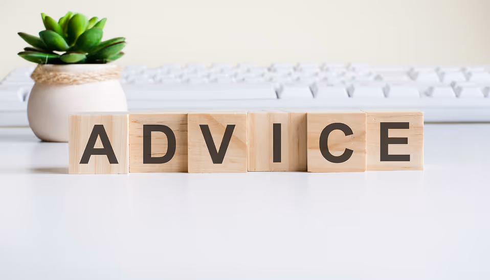 Wooden blocks spelling the word ADVICE on a white desk with a keyboard and small potted plant in the background.