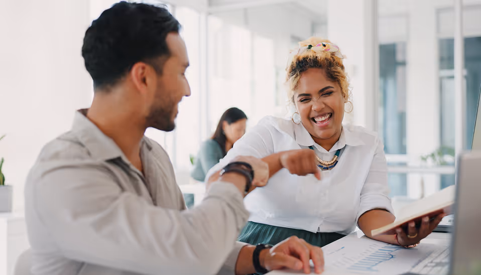 Two colleagues smiling and bumping fists in a bright office while reviewing documents.