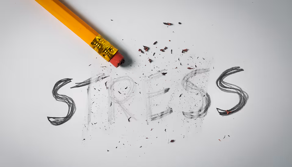 Yellow pencil erasing the word 'STRESS' drawn in pencil on white paper with eraser shavings scattered around.