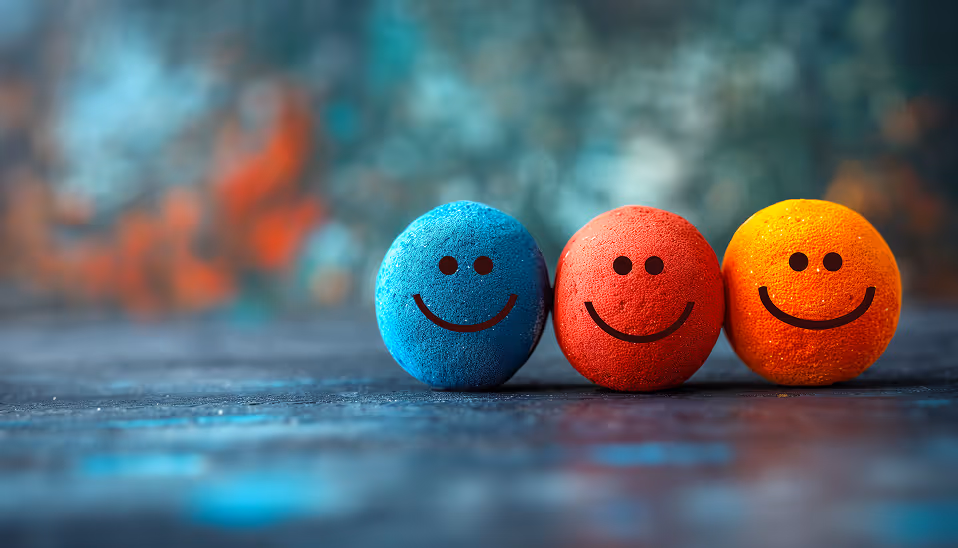 Three colorful stress balls in blue, red, and orange with smiling faces on a blurred background.