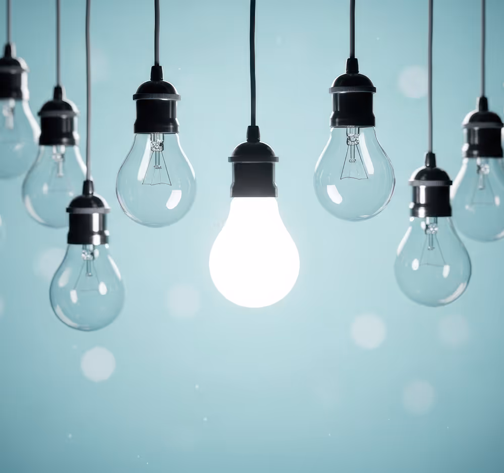 One illuminated light bulb hanging among several unlit bulbs against a blue background.