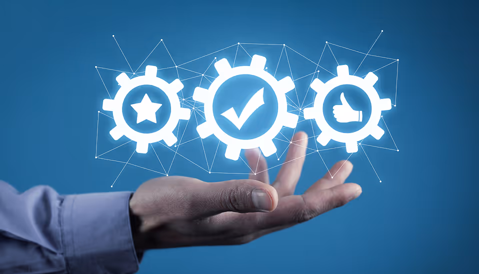A hand beneath three interconnected white gear icons showing a star, a checkmark, and a thumbs-up on a blue background.