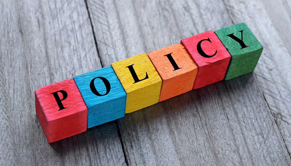 Colorful wooden blocks arranged to spell the word 'POLICY' on a gray wooden surface.