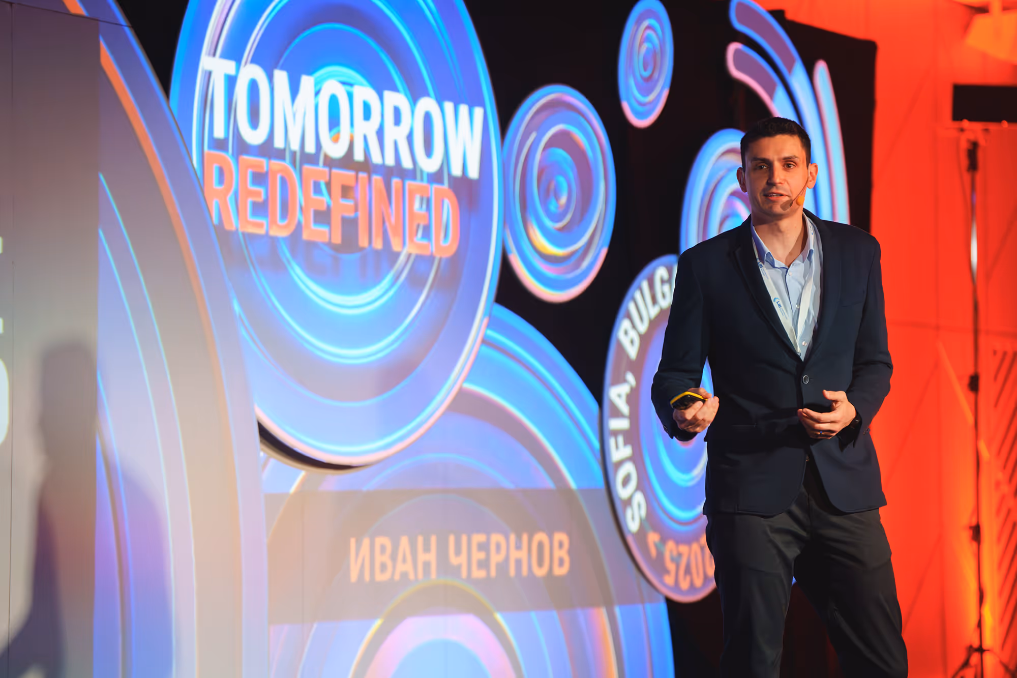 Man in a suit giving a presentation next to a blue circular backdrop with text 'Tomorrow Redefined' and 'Sofia, Bulgaria 2023'.