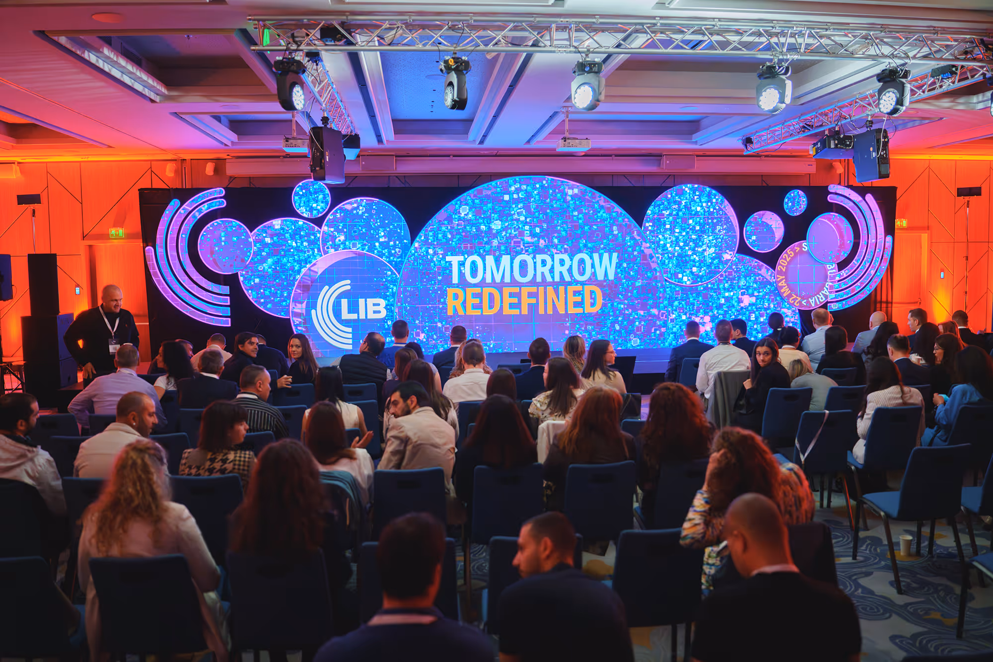 Audience seated facing a large stage with blue circular digital displays and the text 'Tomorrow Redefined'.