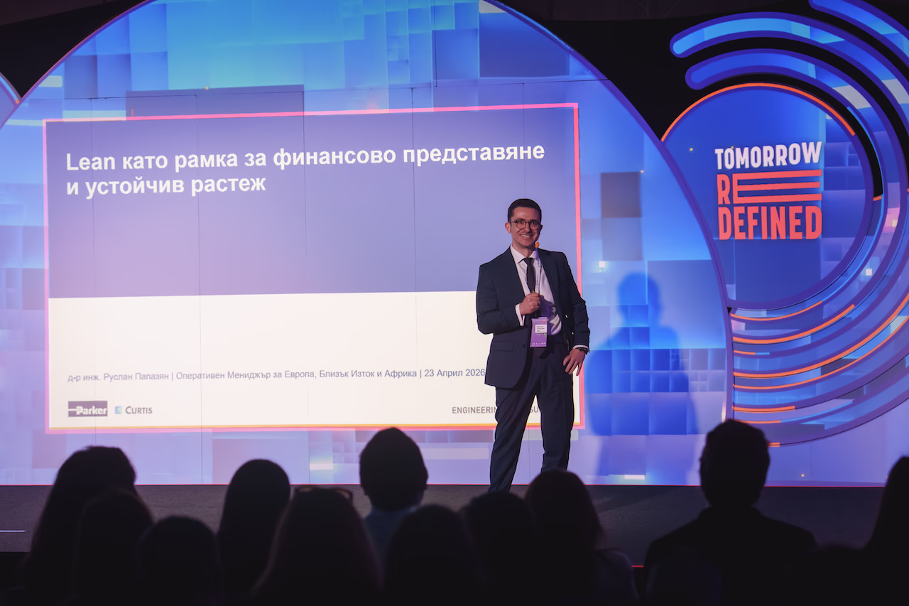 Лектор говори от трибуната на сцената на Tomorrow Redefined пред пълна конферентна зала.